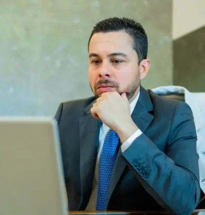 Dr. Lucas Tadeu Moura à mesa do consultório, com a mão no queixo, lendo com atenção a tela do computador