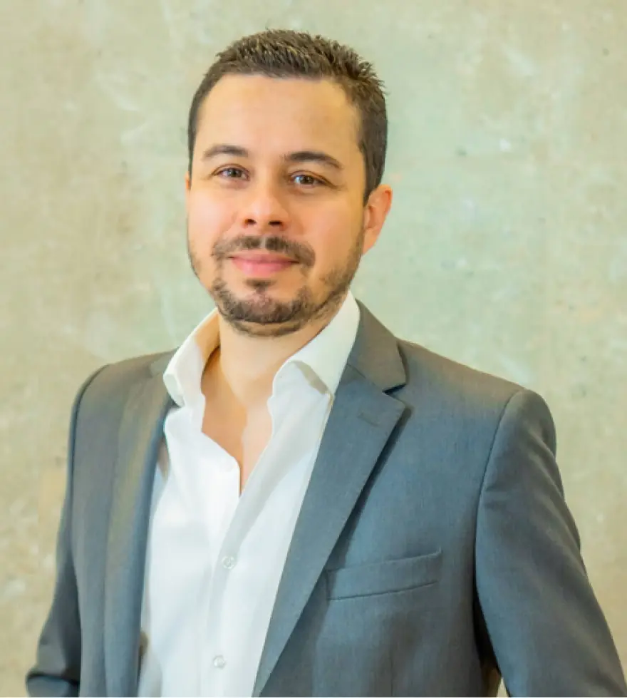 Retrato do Dr. Lucas Tadeu Moura, de terno cinza e camisa branca, sorrindo levemente diante de uma parede clara